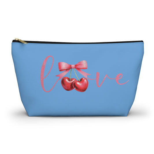 A small blue cosmetic case with a cherry design and the word 'love' printed on the front, featuring a gold-colored zipper closure.