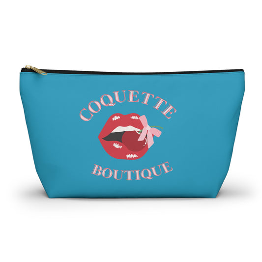 A blue cosmetic case with a 'Coquette Boutique' print on the front and a pink bow detail within the text. The case has a zipper closure.