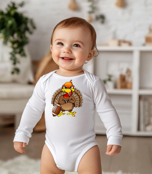 A baby wearing a white long sleeve bodysuit with a Thanksgiving themed design featuring a turkey.