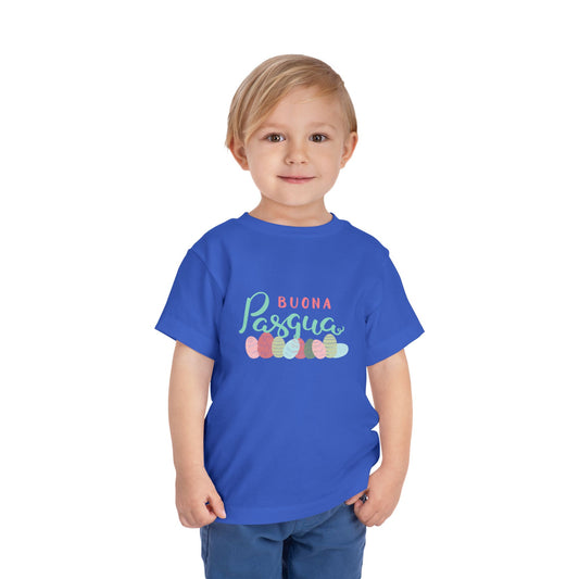 A toddler wearing a blue short sleeve t-shirt with 'BUONA PASQUA' text and colorful Easter egg graphics on the front.