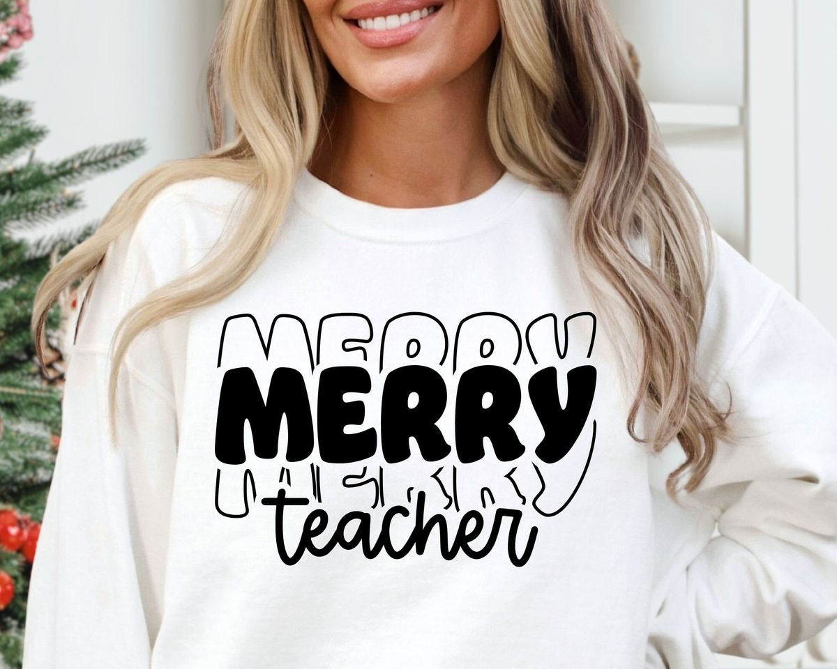 A smiling teacher wearing a white crewneck merry teacher sweatshirt with black text and decorations.