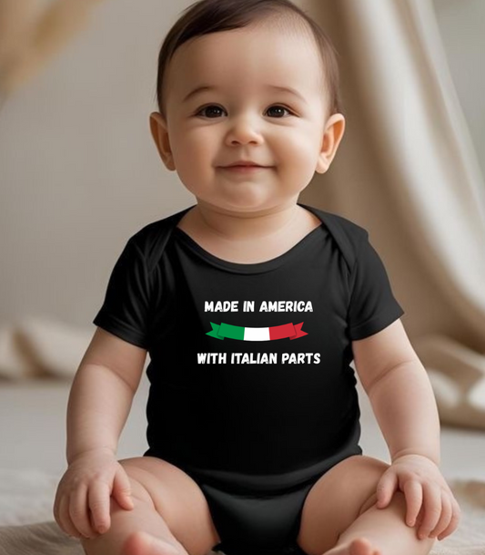 Baby wearing a black onesie with text and flag design, sitting on a light-colored surface.