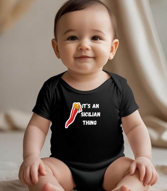 Baby wearing a black onesie with a graphic and text, sitting on a light-colored surface.