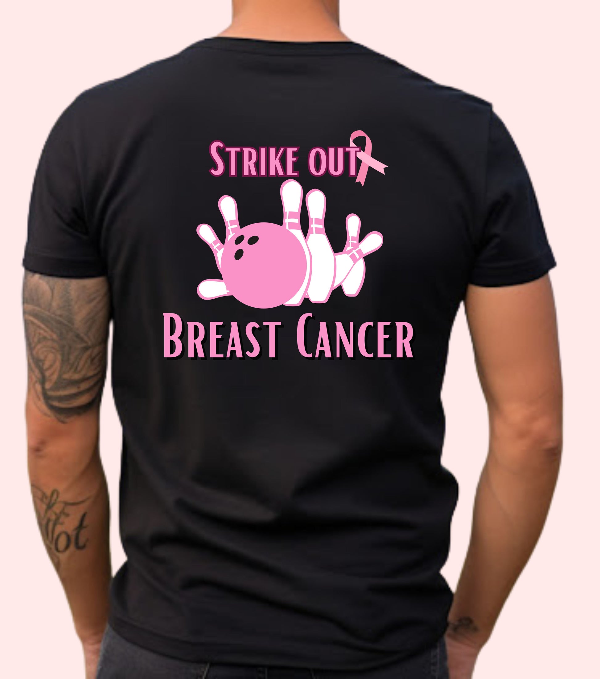 A person wearing a black unisex short-sleeve t-shirt with a pink graphic of a bowling pin and the text 'STRIKE OUT BREAST CANCER' on the front.