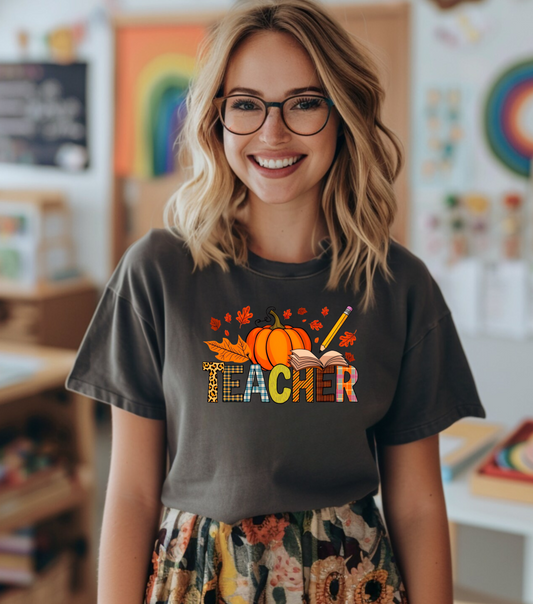 Person wearing a 'Teacher' shirt with pumpkins and books in a classroom setting